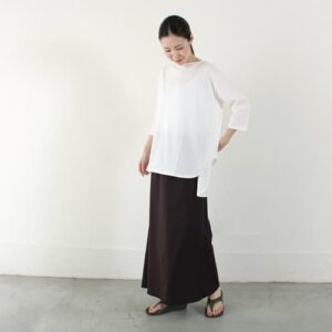白い服と黒っぽいスカートにリカバリーサンダルのコーディネートで着こなす女性
